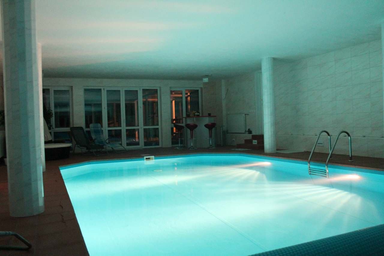 Vnitřní bazén v tyrkysovém osvětlení, lehátka a whirlpool po straně